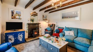 A cozy living room with a fireplace, blue sofa, and a television. - Smithy House (Lochgilphead)