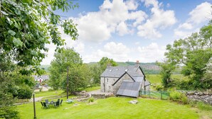 A stone house with a sloped roof, surrounded by a well-maintained lawn and a stone wall. - Smithy House (Lochgilphead)