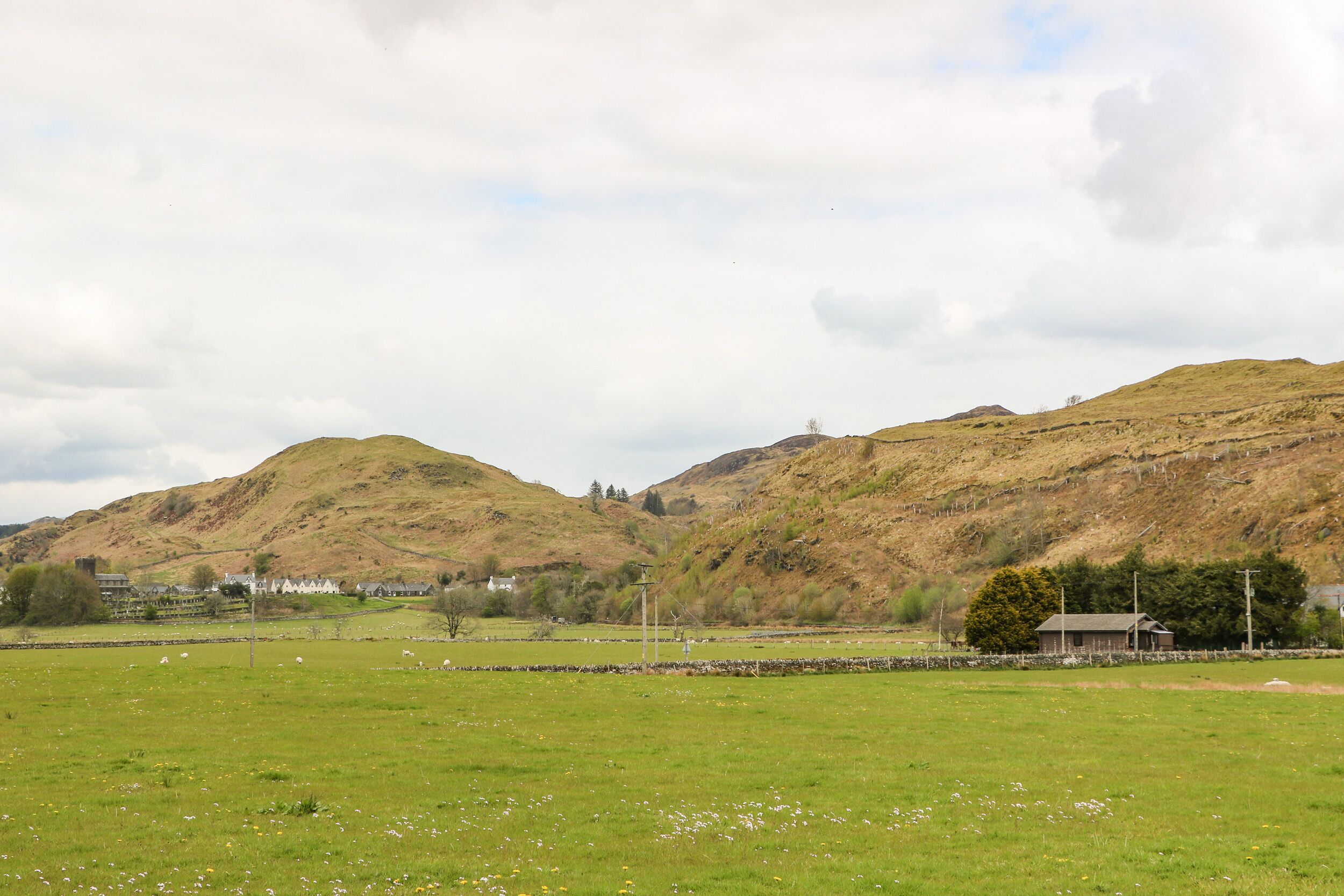 A rural landscape with rolling hills, a grassy field, and a few buildings in the distance.