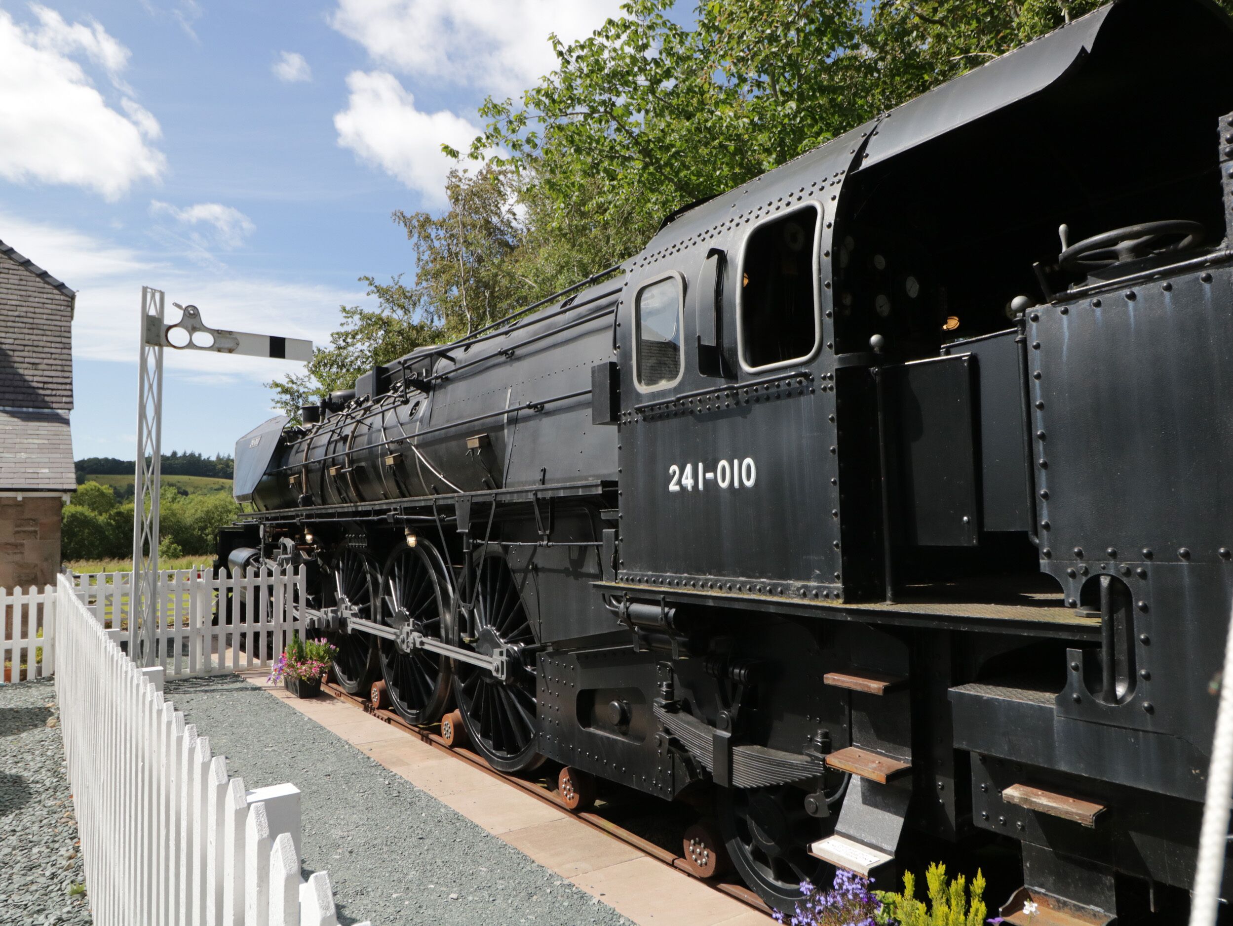 Uma locomotiva a vapor preta com o número 241-010 estacionada sobre os trilhos.