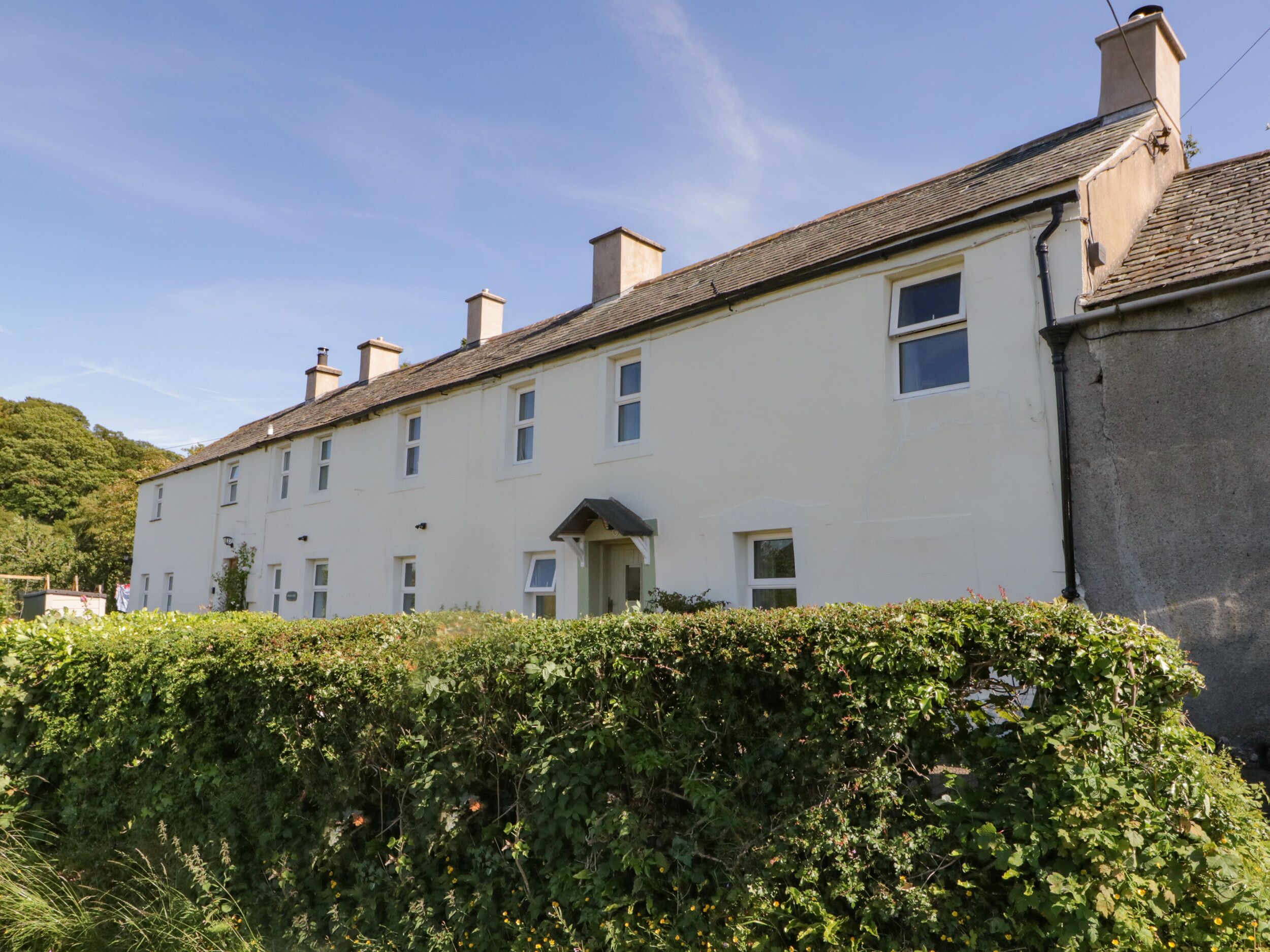 A row of white houses with multiple chimneys, a hedge in the foreground, and a clear blue sky.