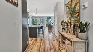 Una cocina moderna con suelo de madera, una isla central, iluminación colgante y vistas al jardín trasero.
