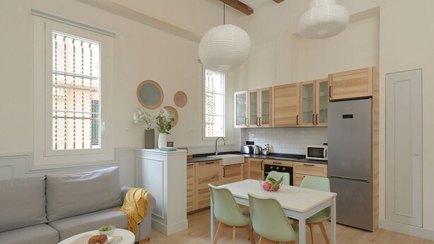 Een moderne keuken met houten kastjes, een roestvrijstalen koelkast en een eethoek met een witte tafel en groene stoelen.