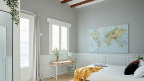 Een slaapkamer met een bed, een bureau, een stoel, een wereldkaart aan de muur en een raam met gordijnen.