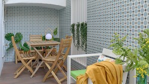 Een terras met een houten tafel en stoelen, een witte bank en een gele plaid.