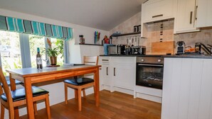 A kitchen with wooden flooring, white cabinets, a dining table with chairs, and a window with curtains.