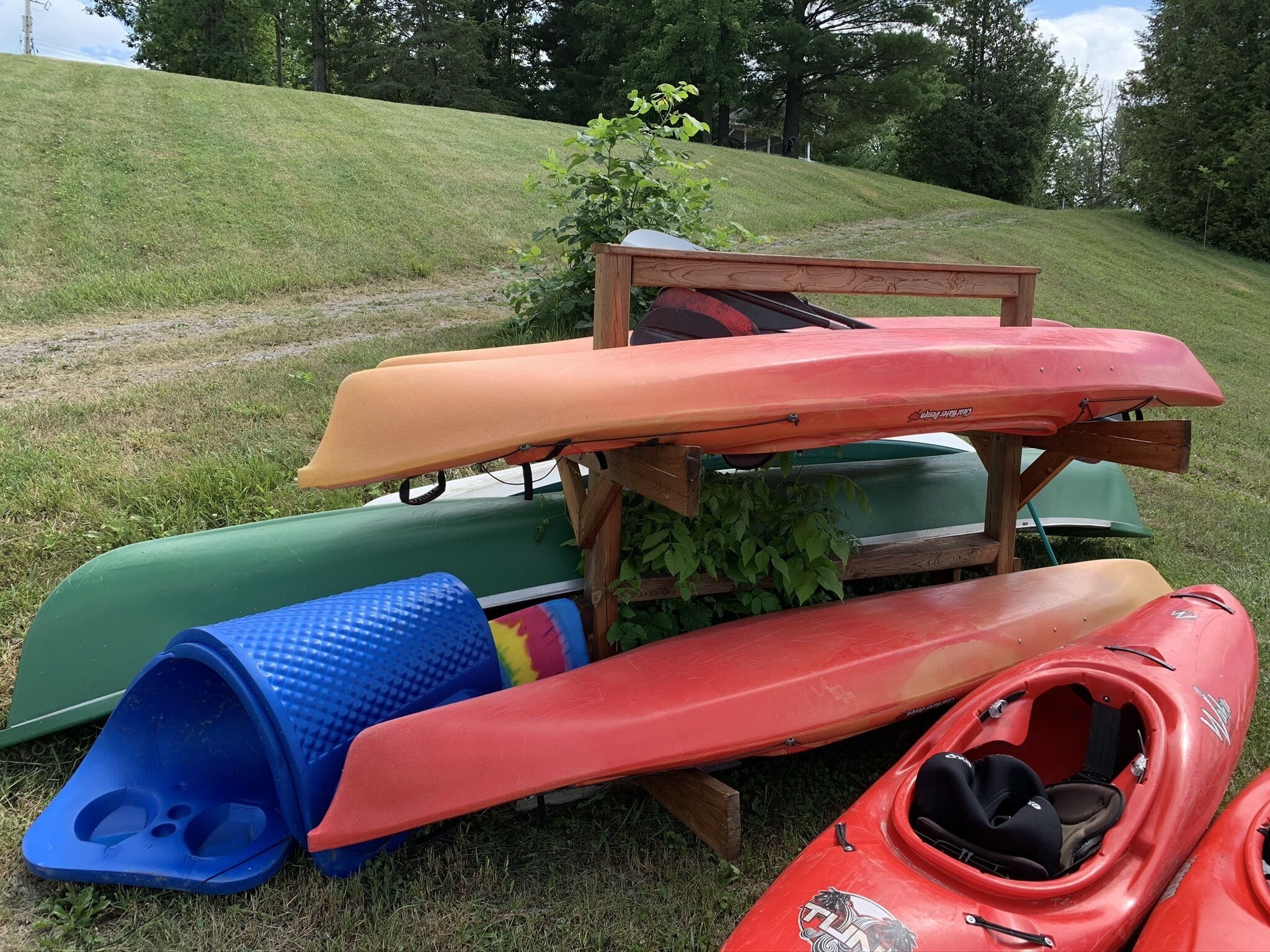 Des kayaks et un grand bac en plastique bleu sur une colline herbeuse.