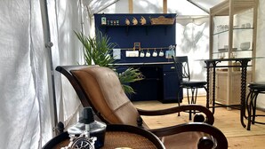 A cozy seating area with a chair, a small table with a decorative item, and a bar area in the background. - Glamping in the Captain’s Quarters! (Wendover)
