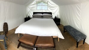 A tented room with a bed, a chair, a bench, and a window. - Glamping in the Captain’s Quarters! (Wendover)