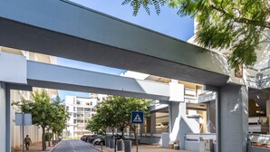 A pedestrian walkway under an overpass with a blue pedestrian sign, trees, and parked cars. - Ciel Apartment, Wifi, Balcony !new! (Tróia)