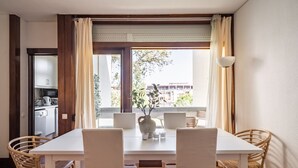 A dining area with a white table and chairs, a vase with flowers, and a view of buildings outside. - Ciel Apartment, Wifi, Balcony !new! (Tróia)