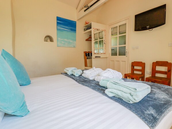 Quarto de hotel com cama, toalhas, televisão e porta com espelho.