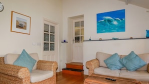 A cozy living room with wicker furniture, a wooden coffee table, and a painting of a wave on the wall. - Abalone (Bude)