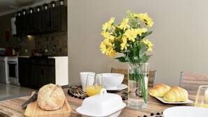 Une table en bois dressée pour le petit-déjeuner, avec du pain, des croissants et un vase rempli de fleurs jaunes.