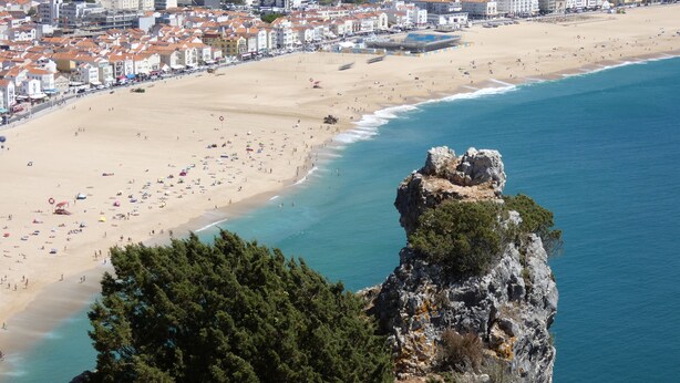 Un paysage urbain côtier avec une plage de sable, un promontoire rocheux et une zone urbaine dense avec des bâtiments.