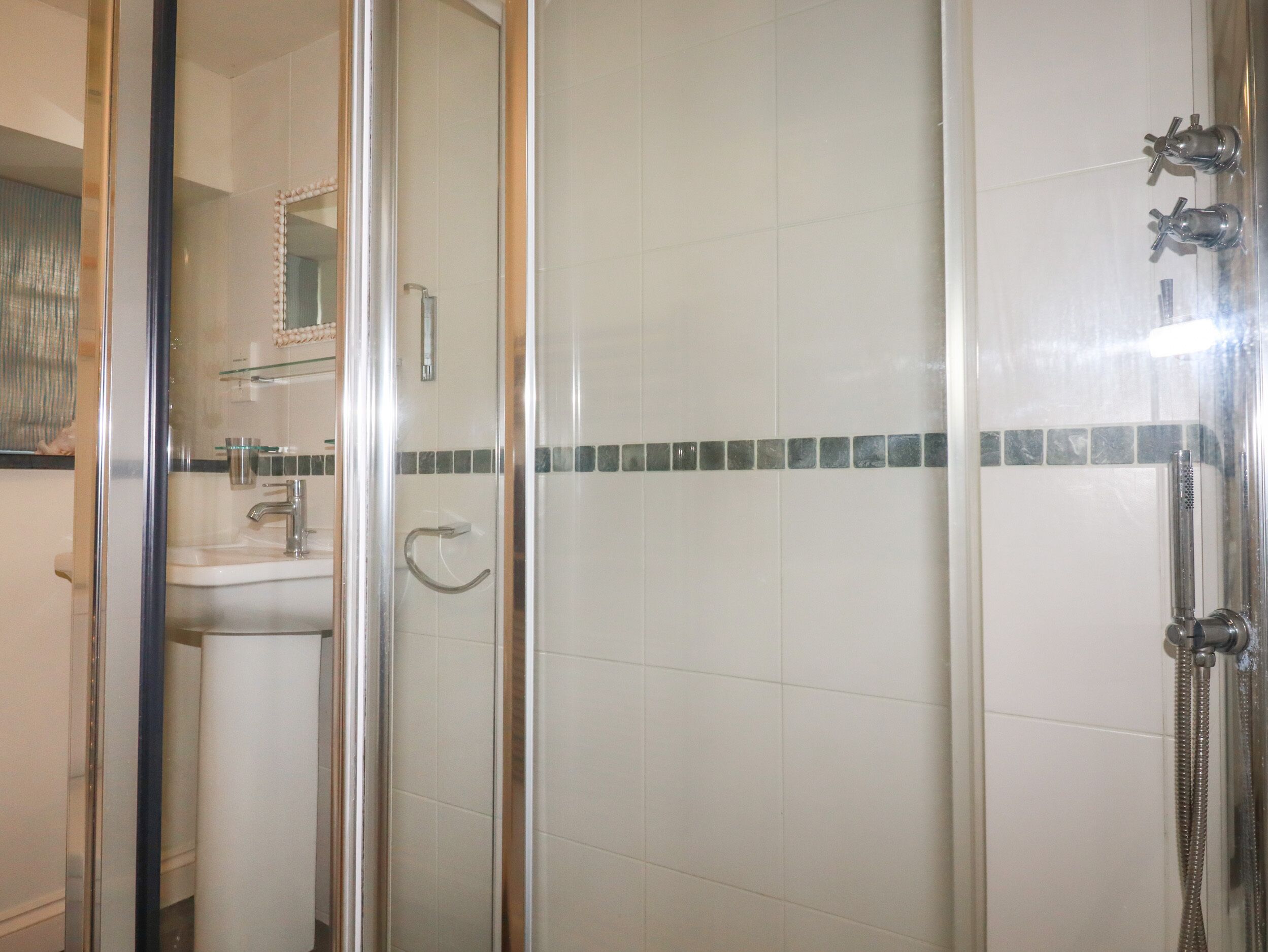 Een badkamer met een glazen douchecabine, een wastafel en een spiegel.