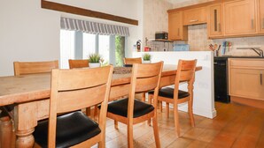 A modern kitchen with wooden cabinets, a white refrigerator, and a dining table with chairs. - Oyster (Bude)