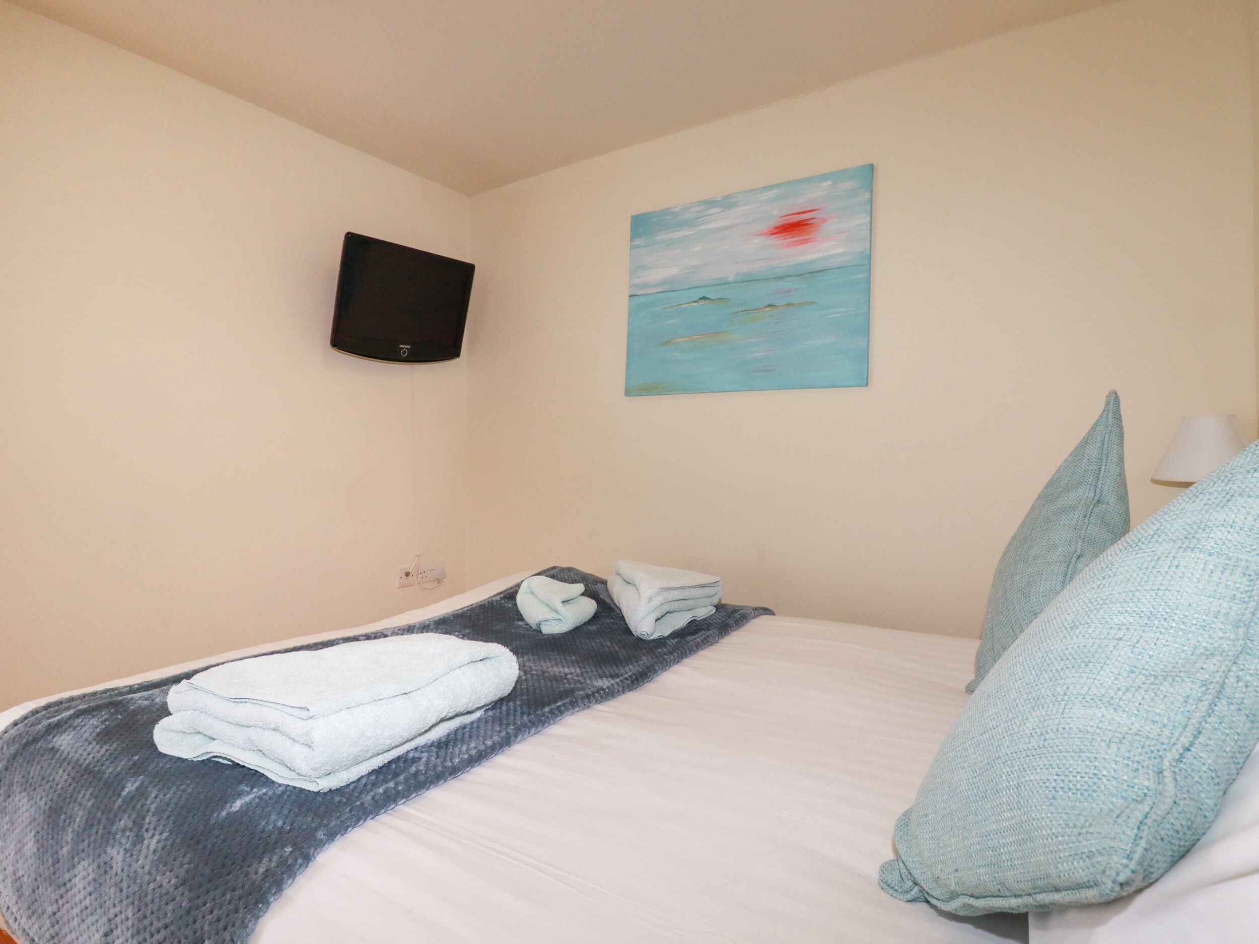Une chambre d’hôtel avec un lit, un téléviseur à écran plat fixé au mur et un tableau au-dessus du lit.