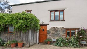 A house with a wooden door, a stone wall, and a brick pathway leading to the entrance. - Oyster (Bude)