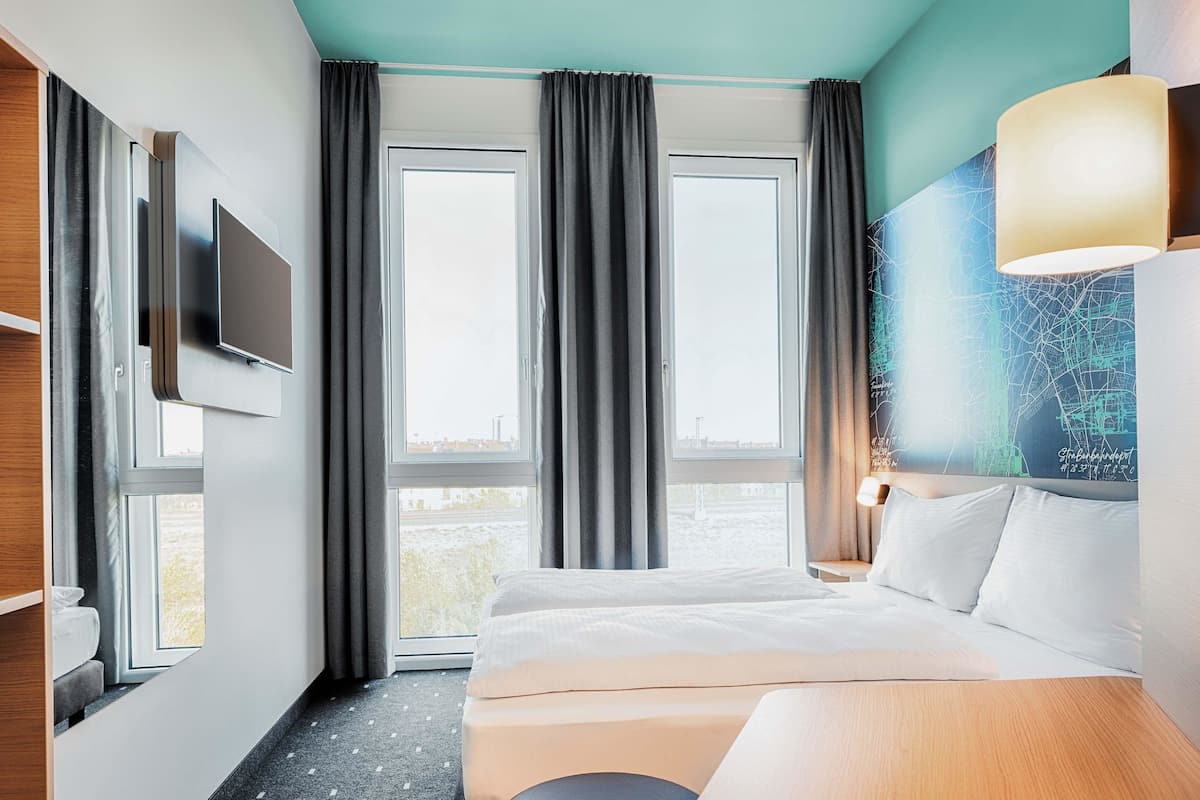 A hotel room with a bed, a desk, a TV, and a large window with curtains.