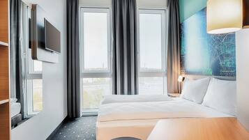 Una habitación de hotel con cama, escritorio, televisión y un ventanal con cortinas.