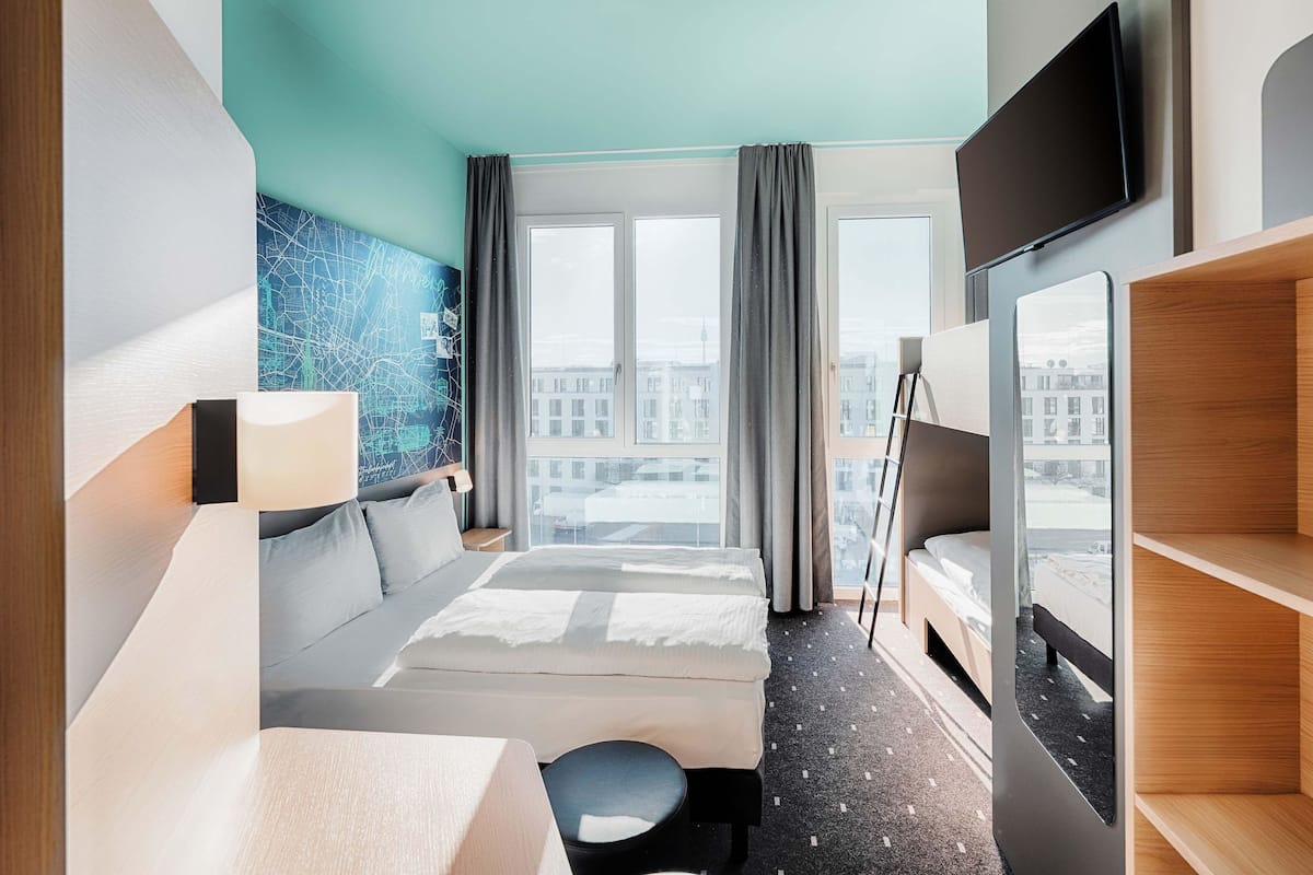 A modern hotel room with a large bed, a desk, a chair, a TV, and a city view through the window.