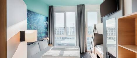 A modern hotel room with a large bed, a desk, a chair, a TV, and a city view through the window.