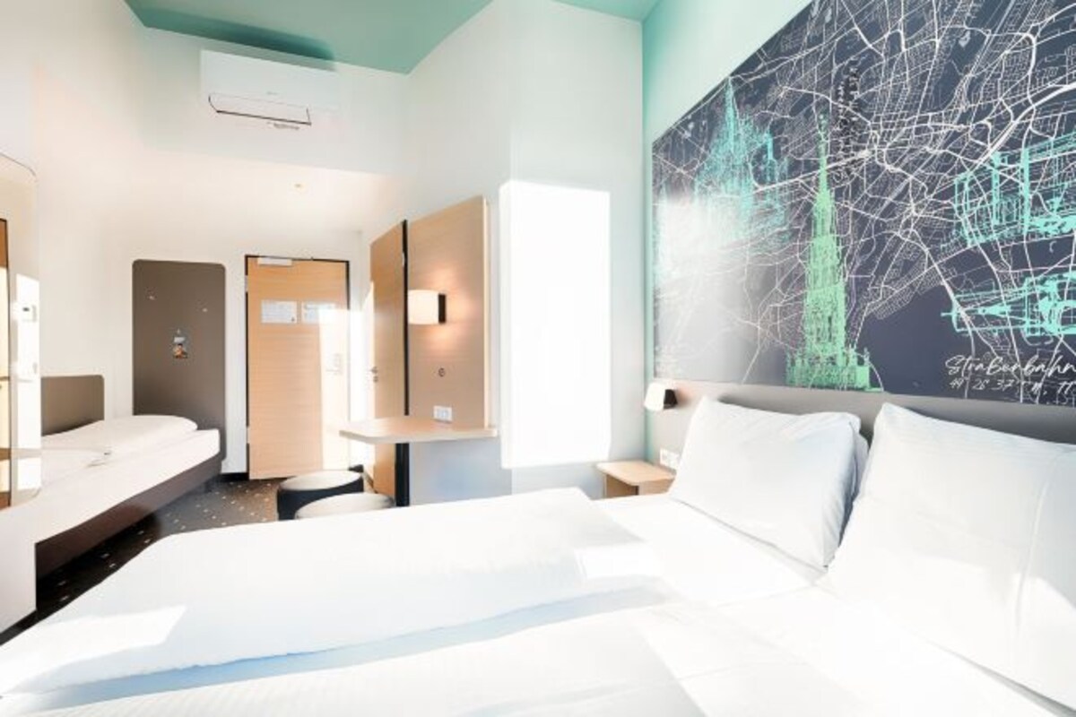 A modern hotel room with a large bed, a desk, and a wall-mounted map.