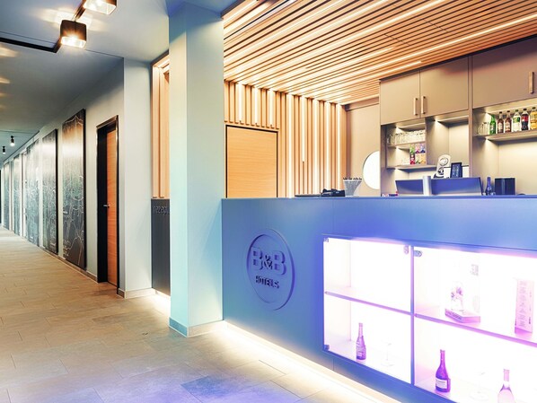 A hotel reception area with a modern design, featuring a reception desk, a minibar, and a wall-mounted clock. - B&B Hotel Nürnberg-West (Nuremberg)