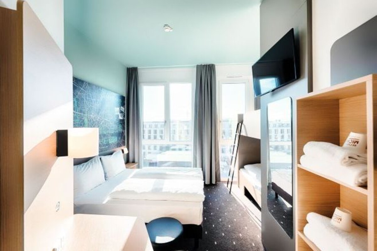 A hotel room with a bed, a desk, a chair, a TV, and a window with curtains.