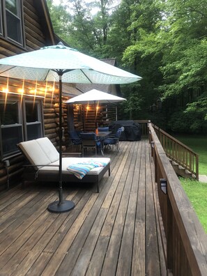 A wooden deck with outdoor furniture, including a lounge chair and a table with umbrellas. - LOG  CABIN IN ZEN FOREST (Wallkill)