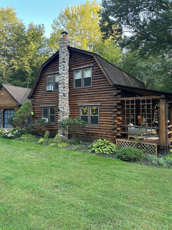 A log cabin with a stone chimney, a porch with seating, and a well-maintained garden. - LOG  CABIN IN ZEN FOREST (Wallkill)