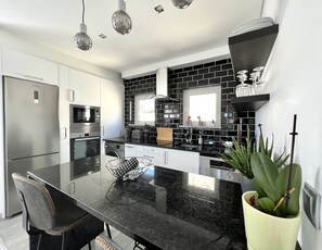 Una cocina moderna con una paleta de colores blanco y negro, electrodomésticos de acero inoxidable y una isla central con asientos.