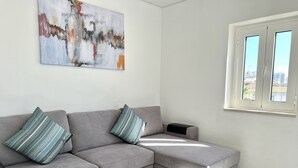 A modern living room with a grey sectional sofa, striped pillows, a white coffee table, and two small potted plants. - Nancy Apartment - Near Vilamoura marina by HD PROPERTIES (Vilamoura)
