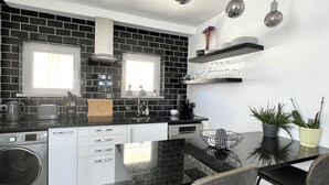 A modern kitchen with black and white tiles, a central island with seating, and pendant lighting. - Nancy Apartment - Near Vilamoura marina by HD PROPERTIES (Vilamoura)