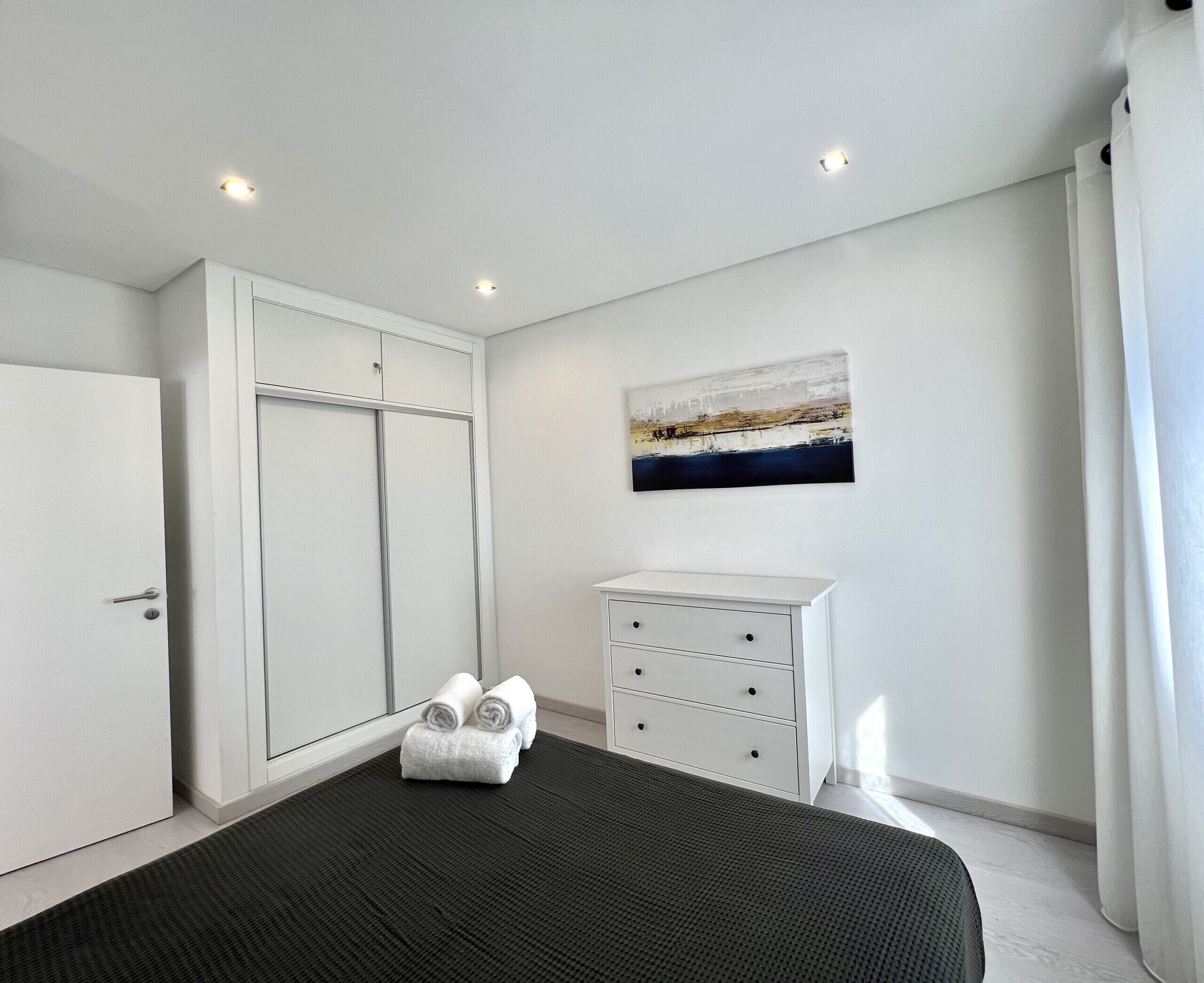 A bedroom with a bed, a wardrobe, a dresser, and a painting on the wall.