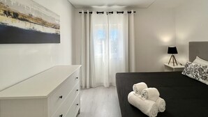 A modern bedroom with a bed, a nightstand, a lamp, and a painting on the wall. - Nancy Apartment - Near Vilamoura marina by HD PROPERTIES (Vilamoura)