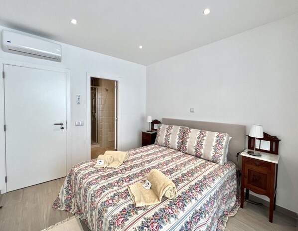 A bedroom with a bed, bedside tables, a nightstand, a door, and an air conditioning unit. - Beachfront apartment—with a pool—from HD PROPERTIES (Quarteira)