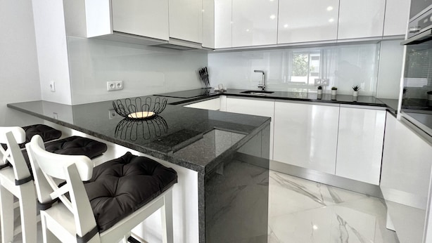 Een moderne keuken met witte kasten, een zwart aanrecht en een marmeren vloer.