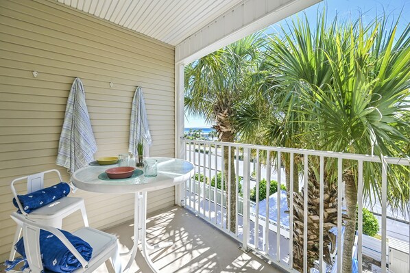 Un balcon avec une balustrade blanche, une petite table sur laquelle se trouvent un bol et un verre, et deux chaises dotées de coussins bleus.