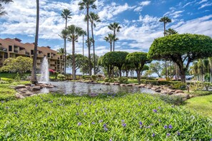 A landscaped garden with a pond, palm trees, and a building with multiple balconies.