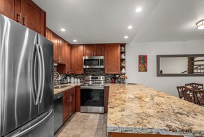 A modern kitchen with stainless steel appliances, wooden cabinets, granite countertops, and a dining area with a large mirror and chairs.