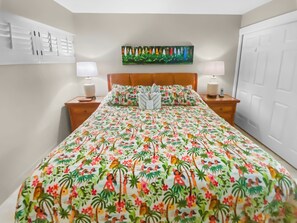 A bedroom with a floral bedspread, two bedside tables with lamps, a headboard, and a painting on the wall.