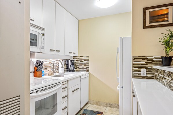 A compact kitchen with white cabinets, a microwave, a sink, and a refrigerator.