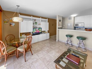 Una cucina moderna con mobili bianchi, un'area pranzo con tavolo in vetro e sedie di legno, e un bancone con sgabelli.