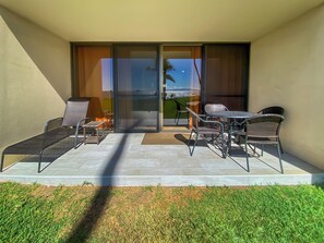 Eine Terrasse mit Gartenmöbeln, Blick durch Glastüren und ein gepflegter Rasen.