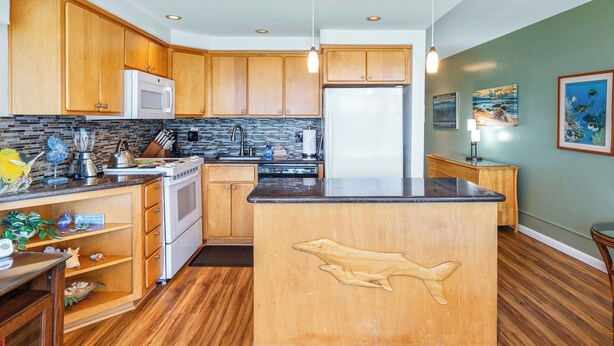 Una cocina con armarios de madera, una isla central con talla de pez, microondas y refrigerador.