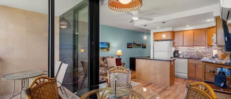 A modern kitchen with wooden cabinets, a dining area with wicker chairs, and a glass table.