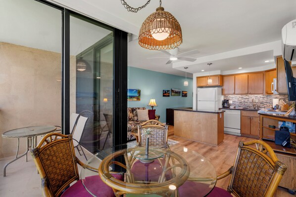 A modern kitchen with wooden cabinets, a dining area with wicker chairs, and a glass table.