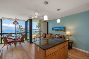 A spacious living area with a view of the ocean, a dining table with chairs, a sofa, and a kitchen island.